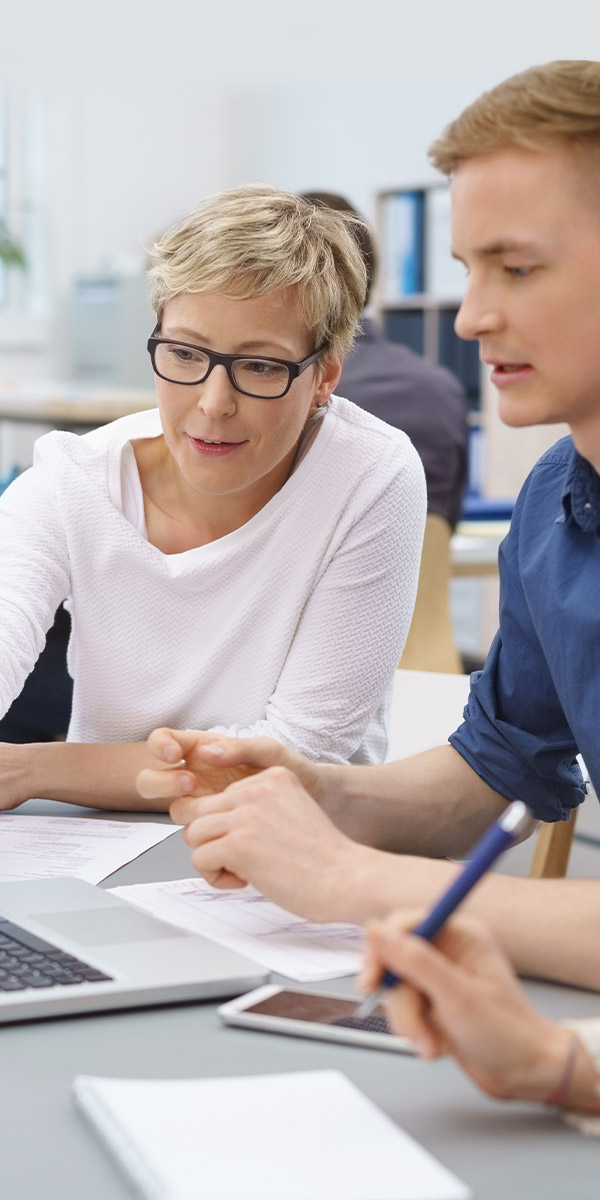 Drei Personen sitzen an einem Tisch vor einem Computer und unterhalten sich